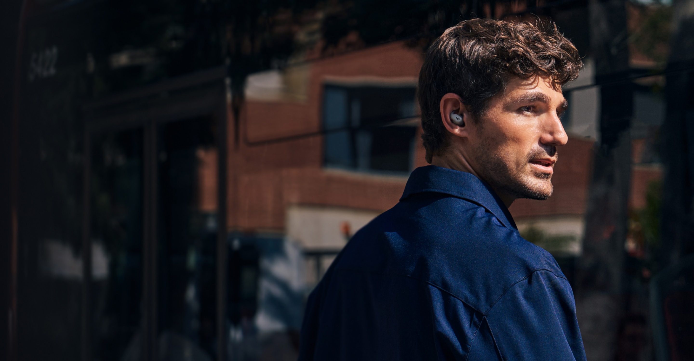 Man wearing Gravel Gray Powerbeats Fit earbuds on a sunny city street