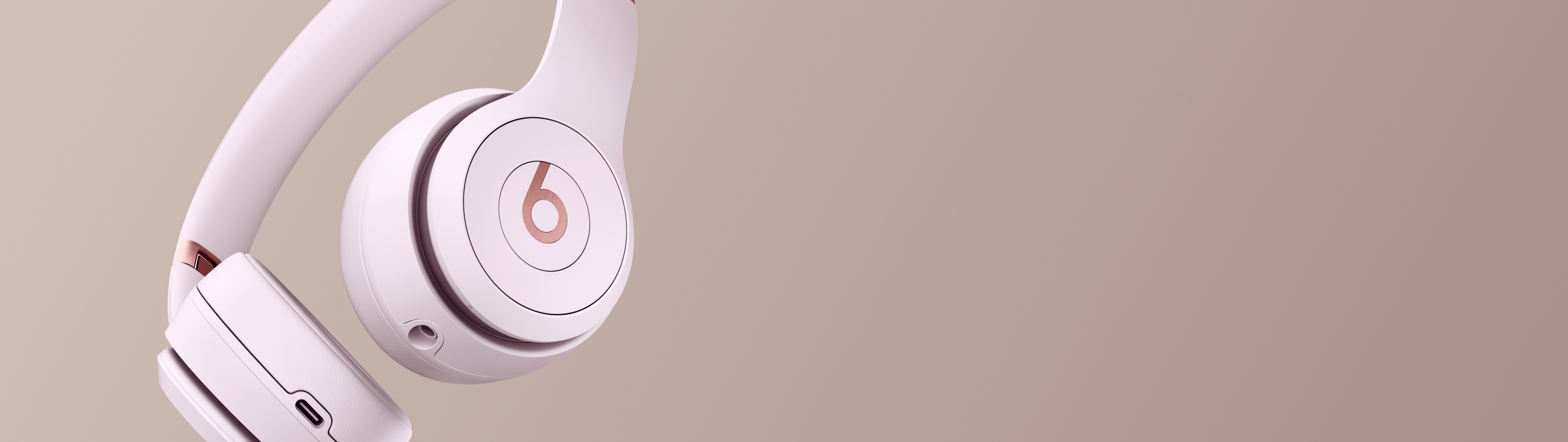 Beats Solo 4 headphones in Cloud Pink angled against a warm mauve background